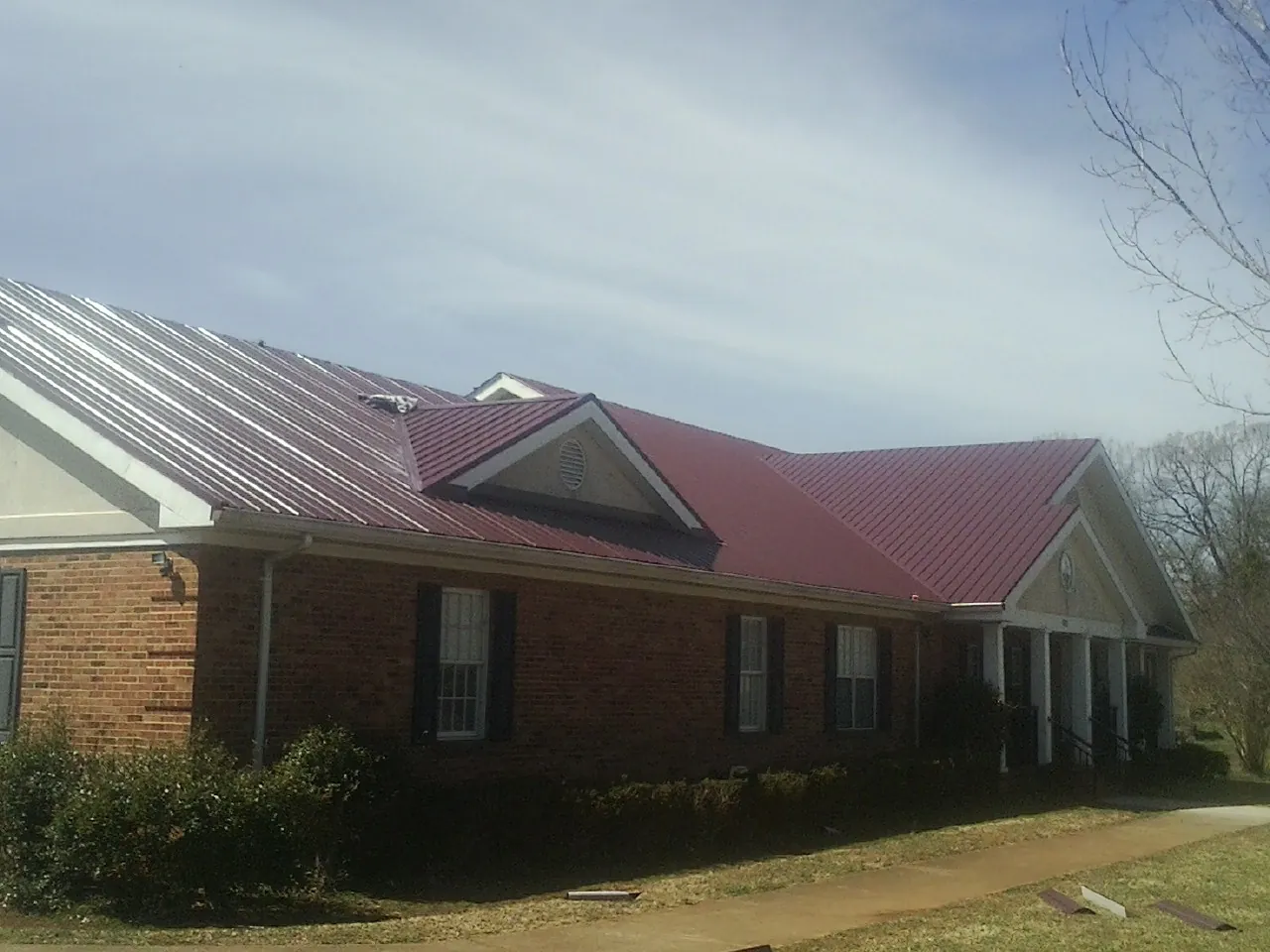 Red metal roof with gabled entries on a long brick building, from a Hail Damage Roof Repair job in Spruce Pine