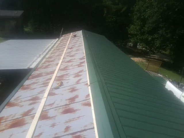Old rusted panels beside newly installed green metal roofing — Wind Damage Roof Repair by Roofing Brothers in Spruce Pine
