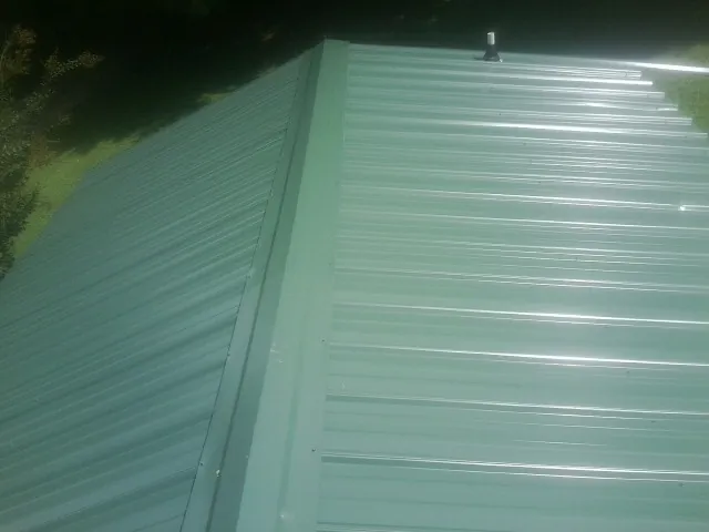 New green metal panels meeting at the ridge of a roof — Flat Roof Repair work by our crew in Spruce Pine