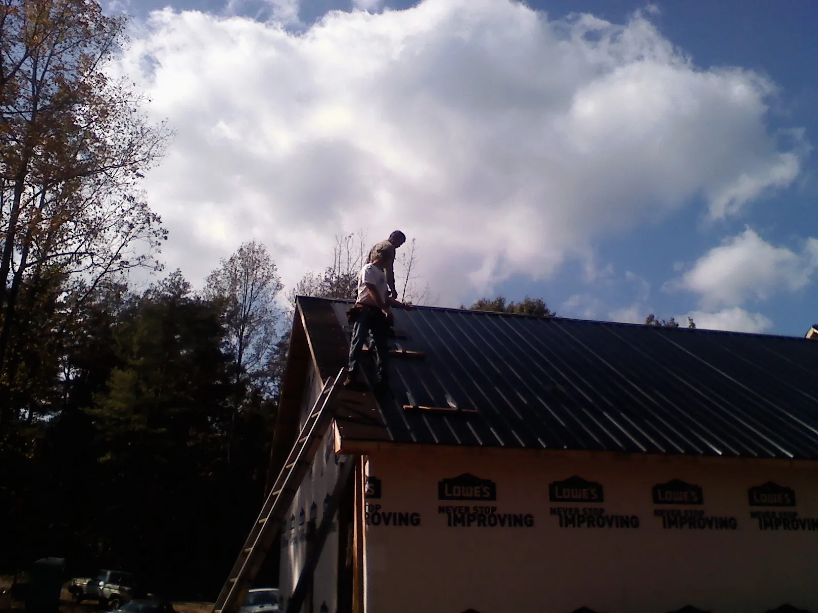 Roofer fastening dark metal panels high against a cloudy sky, from a Roof Inspection job in Spruce Pine